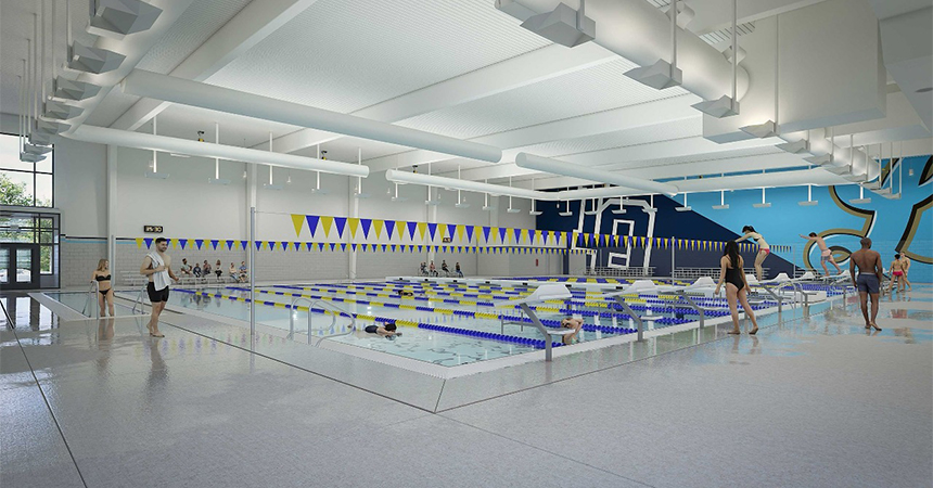 Indoor swimming pool facility with multiple lanes separated by blue and white dividers. Yellow and blue triangular flags hang above the pool. Swimmers are in the water, and others stand or walk along the pool deck. The space is brightly lit with white ceiling panels and large windows. A mural with abstract shapes and a stylized figure decorates the far wall. Starting blocks at each lane suggest competitive use.