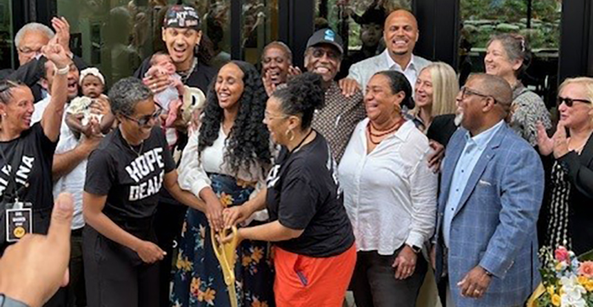 A group of people gather outside the new Albina One multifamily housing community to celebrate the grand opening with a ribbon cutting.