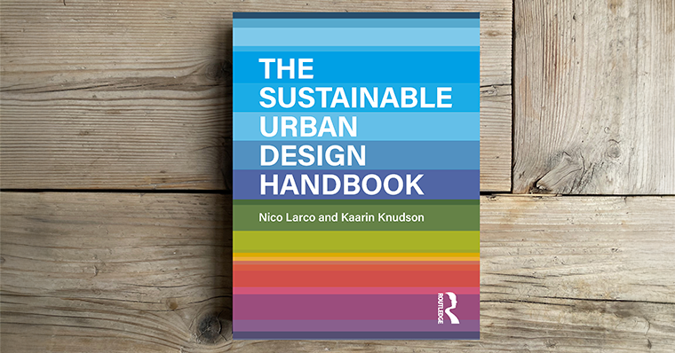 A book titled The Sustainable Urban Design Handbook lies on a wooden surface. The cover features horizontal stripes in vibrant shades of blue, green, orange, red, and purple. The title is displayed in large white and purple text across the top half, with authors Nico Larco and Kaarin Knudson listed below in white on a green stripe. The Routledge publisher logo appears in white at the bottom right corner.